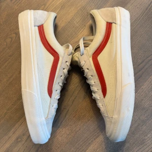 Vita Vans sneakers med röd sidodetalj - Säljer ett par klassiska vita Vans sneakers med den ikoniska röda sidoremsan. Skorna är knappt använda pga fel storlek. Endast några fläckar på sulan (vilket syns på bilderna). Perfekta för en avslappnad och stilren look.