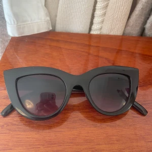 Svarta cat eye solglasögon från NA-KD - Stilrena svarta solglasögon i cat eye-modell från NA-KD. Bågarna är blanka och markerade, vilket ger en trendig look. Perfekta för att lyfta vilken outfit som helst.