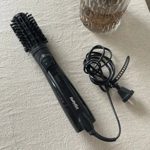 Svart varmluftsborste från BaByliss - En svart varmluftsborste från BaByliss med rund borste och borststrån i plast. Perfekt för att styla och forma håret med volym. Utrustad med sladd och två knappar för olika inställningar.