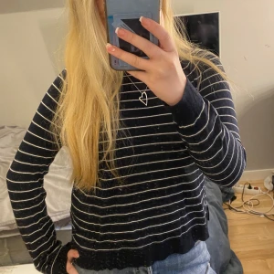 Mörkblå långärmad randig tröja - Säljer en långärmad tröja med tunna vita ränder. Tröjan har en klassisk passform och rund halsringning. Perfekt till jeans eller kjol för en enkel och stilren look.