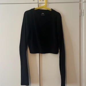 Svart croppad långärmad topp från H&M - Säljer en svart croppad långärmad topp från H&M. Enkel och stilren design med rund halsringning och mjukt bomullsmaterial. Perfekt att matcha med höga jeans eller kjol. Snygg och basic för en trendig look.