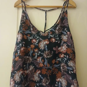 Blommig linnetopp från Amisu - Säljer en blommig linnetopp från Amisu i mörkblått med bruna och vita blommor. Toppen har smala axelband och en snygg detalj i ryggen. Perfekt för varma dagar och enkel att matcha med jeans eller kjol.