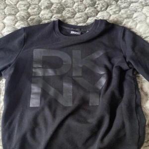 Svart sweatshirt från DKNY - Säljer en svart sweatshirt från DKNY med stor logga framtill. Tröjan har rund halsringning och långa ärmar. Perfekt för en stilren och avslappnad look.