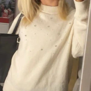 Vit stickad tröja med pärlor från H&M - Säljer en vit stickad tröja från H&M med pärldetaljer framtill. Tröjan har lång ärm, ribbad mudd vid hals, ärmslut och nederkant. Perfekt för dig som gillar en mysig och stilren look.