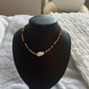 Färgglatt halsband med pärla - Ett halsband med små, färgglada pärlor i olika nyanser och en större vit pärla i mitten. Perfekt för att ge en lekfull touch till din stil.