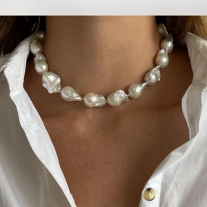 Chunky pärlhalsband med barockpärlor - Unikt halsband med stora, vita barockpärlor. Halsbandet har en dekorativ knäppning och ger ett statement-utseende. Perfekt för dig som vill sticka ut med ett trendigt och elegant smycke.