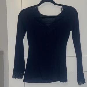 Svart långärmad topp med spetsdetaljer från Intimissimi - Säljer en svart långärmad topp från Intimissimi med v-ringning och fina spetsdetaljer vid halsringning och ärmslut. Tunn och mjuk i materialet, perfekt för lager-på-lager eller som den är.