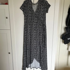 Svart blommig omlottklänning från & Other Stories - Säljer en svart omlottklänning från & Other Stories i storlek XS. Klänningen har vitt blommönster, v-ringning och korta ärmar. Perfekt för vår och sommar med sin luftiga känsla och fina passform.