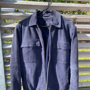 Mörkblå mockajacka från Human Scales - Säljer en stilren mörkblå mockajacka från Human Scales. Jackan har klassisk krage, två stora bröstfickor och dragkedja framtill. Utsidan är i 100% äkta mocka och fodret i polyester. Perfekt jacka för både vår och höst. Nypris 3000kr