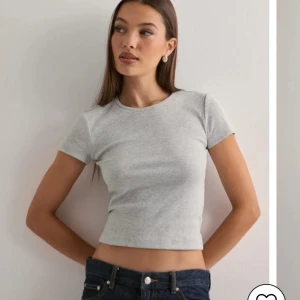Ljusgrå ribbad croppad t-shirt - Säljer en ljusgrå croppad t-shirt med ribbad struktur. T-shirten har rund halsringning och korta ärmar. Perfekt för en enkel och stilren look.