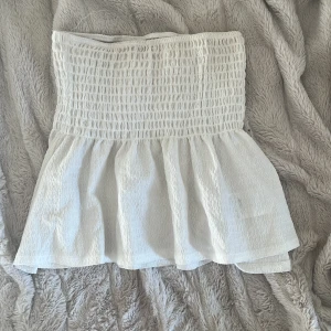 Vit smockad volang  tubtopp från Gina Tricot - Säljer en söt vit volang tubtopp från Gina Tricot med smockad överdel och volang nertill. Perfekt för varma dagar och enkel att matcha med både jeans och kjol. Nypriset var 279 kr men den säljs för 150 kr. Skriv privat för bilder på💞😸🫰😝