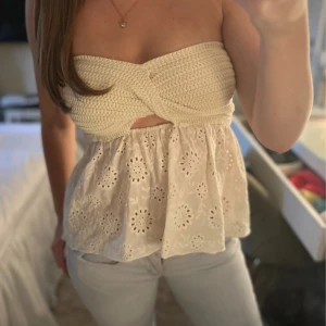 Vit axelbandslös croppad topp - Säljer en söt axelbandslös topp i vitt med virkad överdel och broderad, luftig nederdel. Toppen är croppad och har ett twistat parti framtill. Är i nyskick från Zara💗☺️