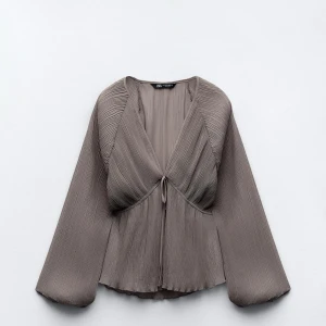 Ljuslila blus med knyt och vida ärmar - Säljer en ljuslila blus med plisserat tyg och knyt framtill. Blusen har långa, vida ärmar och är lätt transparent.