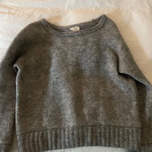 Grå stickad tröja med rund hals - Mysig grå stickad tröja med rund halsringning och ribbade muddar vid ärmslut och nederkant. Perfekt för kyligare dagar och enkel att matcha med olika outfits. Strl M men passar S även.