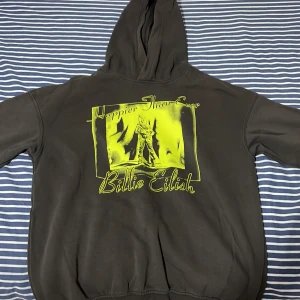 Svart Billie Eilish hoodie från H&M - Cool svart hoodie från H&M med stort gult tryck av Billie Eilish och texten 'Happier Than Ever' på framsidan. Mjuk insida och huva, perfekt för dig som gillar streetstyle och vill sticka ut med en unik tröja.