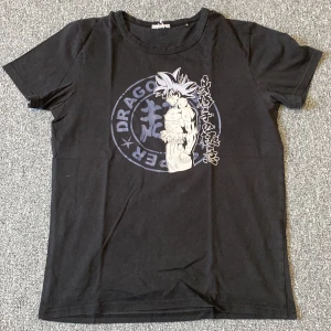 Svart Dragon Ball t-shirt Goku motiv - Svart t-shirt med tryck av Goku från Dragon Ball på framsidan. Klassisk rund hals och korta ärmar. Stort anime-motiv i grått och vitt med japansk text och logga. Hör av dig efter frågor och fler bilder.