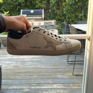 Golden Goose vita sneakers  - Snygga vita sneakers från Golden Goose med grå mockadetaljer och ikonisk stjärna på sidan. Skorna har grå snörning, blå hälkappa och platt sula. 