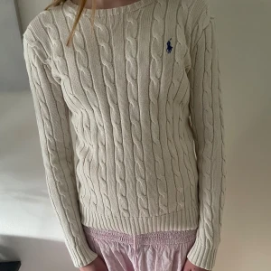 Kabelstickad tröja Polo Ralph Lauren XS - Kabelstickad, krämvit tröja från Polo Ralph Lauren med klassisk blå logga på bröstet. Tröjan har rund halsringning, ribbade muddar och lång ärm. Säljer då den inte riktigt är min stil. 