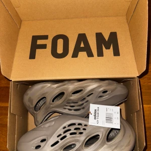 Adidas Yeezy Foam Runner ”Stone Age” - Adidas Yeezy Foam Runner ”Stone Age” i en grå, marmorerad färg. Skorna har en futuristisk design med många öppningar och en chunky, vågig sula. Tillverkade i lätt syntetmaterial som ger en unik look och känsla. Perfekta för dig som vill sticka ut med något annorlunda i sommar. Storlek eu 43, us 9, uk 9. Helt oanvända, dvs DSWT, och original låda medföljer. Priset är aningen förhandlingsbart. 