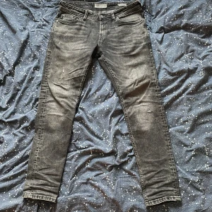 Grå slim jeans Tom Tailor W30 L32 - Snygga grå jeans från Tom Tailor i modellen Piers Slim. Jeansen har en tvättad look. Tillverkade i återvunnen bomull för en schysst vibe. Perfekta till sneakers och hoodie.