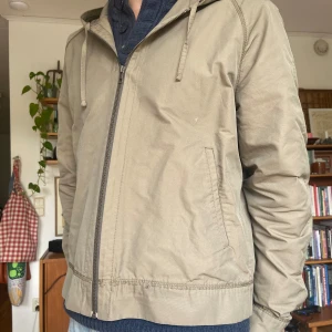 Lanvin vindjacka från milano - Säljer en  beige lanvin vindjacka med huva och hel dragkedja framtill. Jackan har två fickor på sidorna och ribbad mudd nedtill och vid ärmslut. Den har användts kanske tre gånger men köptes second hand i milano så den har lite små slitningar i sömmarna. 