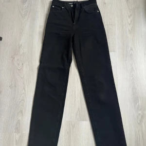 Svarta 90s straight jeans midja 25 - Svarta jeans med rak passform och hög midja i klassisk 90-talsstil. Jeansen har fem fickor, bälteshällor och dragkedja. Snygga till sneakers eller boots och passar perfekt till en avslappnad look.