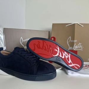 Mörkblå sneakers från Christian Louboutin - Snygga mörkblå sneakers från Christian Louboutin i mocka med klassisk röd sula och broderad logga på hälen. Skorna har rund tå, snörning och diskreta detaljer som ger en lyxig känsla. Perfekta för dig som vill sticka ut med stil.