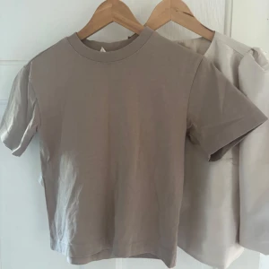 Beige basic t-shirt från Gina Tricot - En stilren beige t-shirt från Gina Tricot, basically basics-kollektionen. T-shirten har rund halsringning med ribbad kant och klassisk passform. Perfekt för en clean och enkel look, lätt att matcha med allt.