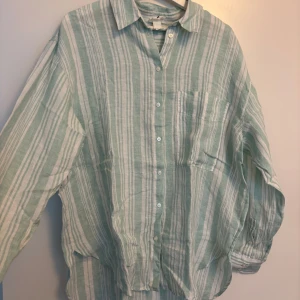 Randig linneskjorta Lemlem x H&M - Snygg oversized skjorta från Lemlem x H&M i ljusgrönt och vitt med randigt mönster. Skjortan är i luftigt linne, har långa ärmar, bröstficka och knappar framtill. Perfekt för en chill och stilren look.