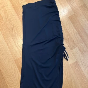 Mörkblå långkjol med snörning - Snygg mörkblå långkjol med dragsko och snörning och slits på sidan som ger en cool rynkad effekt. Kjolen har en enkel och stilren design, perfekt att styla med sneakers eller boots. Materialet känns mjukt och följsamt.❤️