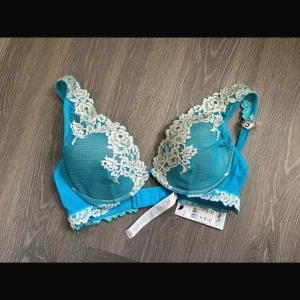 Turkos spets-bh från Intimissimi - Superfin turkosblå bh från Intimissimi med fina spetsdetaljer över kuporna och axelbanden. Bh:n har justerbara axelband och hakknäppning bak. Vadderade kupor. Perfekt för dig som vill ha något extra snyggt under kläderna. Helt ny och oanvänd! Säljes pga felköp till min dotter, den passade ej. 
