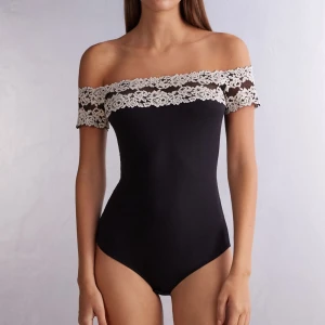 Mörkblå offshoulder body med spets - Säljer en mörkblå offshoulder body  med snygga vita spetsdetaljer i blommigt mönster över axlarna. Toppen är tight och har en stilren, feminin look som passar perfekt till jeans eller kjol. Materialet känns mjukt och stretchigt Och är köpt från intemissmi. Storlek M/L men är liten i storlek och passar S/M💕💕