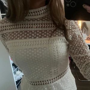 Vit spetsblus med lång ärm - Superfin vit blus i spets med hög hals och lång ärm. Blusen har genombrutna detaljer och markerad midja, samt vackra spetsmönster över hela plagget. Perfekt för dig som gillar romantisk och trendig stil.