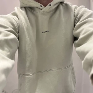 Ljusgrön  hoodie från Selected Homme - Snygg ljusbeige hoodie från Selected Homme med minimalistiskt tryck 'HOMME' på bröstet. Klassisk känguruficka, huva med metallöljetter och mjukt bomullsmaterial. Perfekt för chill dagar och enkel att matcha med jeans eller joggers.