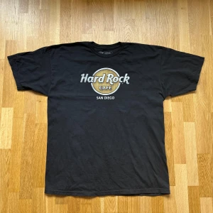Hard Rock Cafe San Diego Svart T-Shirt - Hard Rock Cafe T-Shirt med tryck i färgen Svart. Storlek: XL, Armhåla till Armhåla: 61 cm, Längd: 77 cm, Axel till Armöppning: 22 cm.  Material: 100% Cotton.