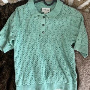 Mintgrön stickad pikétröja Monki - Superfin mintgrön pikétröja från Monki i stickat material. Tröjan har korta ärmar, krage och tre knappar framtill. Snyggt hålmönster över hela tröjan och ribbade muddar vid ärmslut och nederkant. Perfekt för en fräsch och trendig look!