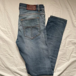 Ljusblå tiger of sweden jeans med fin fade/slitning - Säljer ett par blå slim fit jeans tiger of sweden med snygg ljus tvätt. Jeansen har normal midja och raka ben, med diskreta slitningar för en cool look. Storlek 31-34, jag är 193cm 77kg och skulle säga att de är lite för korta för mig så någon runt 185-187 skulle vara perfekt.