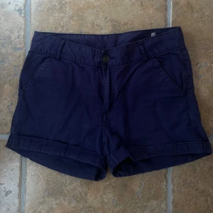 Mörkblå chinosshorts - Snygga mörkblå shorts i bomull med klassisk design. De har två sidofickor fram och två passpoalfickor bak, samt uppvikta benslut. Stängs med knapp och dragkedja. Perfekta för varma dagar och enkel att matcha med det mesta.