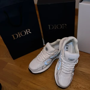 Dior B30 vita sneakers med silverdetaljer - Säljer ett par Dior B30 sneakers i vitt med snygga silverdetaljer och reflekterande partier. Skorna har en chunky sula, mesh och skinnpaneler samt tydlig Dior-logga på sidan. Perfekta för dig som vill sticka ut med exklusiva och trendiga sneakers. Dustbag medföljer!