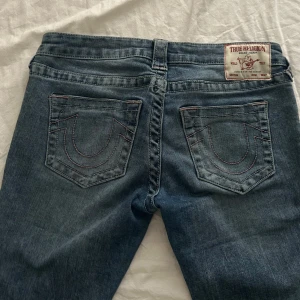 True Religion bootcut jeans blå - Snygga blå jeans från True Religion med bootcut-modell och klassiska kontrastsömmar på bakfickorna. Jeansen har låg midja och är tillverkade i mjukt denim med lätt tvättad look. Perfekta för dig som gillar en avslappnad men trendig stil. Priset kan diskuteras