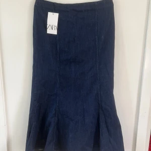 Mörkblå jeanskjol från Zara - Snygg mörkblå långkjol i jeans från Zara. Kjolen har en klassisk rak passform med lätt utsvängd nederdel och är tillverkad i kraftigt denimtyg. Perfekt för dig som gillar stilrena och tidlösa plagg.