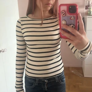Randig långärmad topp i bomull - Säljer en ribbad långärmad topp med svart-vita ränder. Modellen är tight och har rund halsringning. Perfekt till jeans eller kjol och superenkel att styla för en clean look. Materialet är mjuk bomull som känns skönt mot huden.