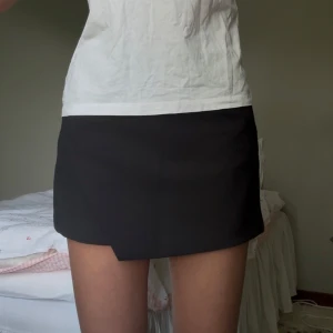 Svart kostymkjol - Supersnygg svart kostymkjol från Zara med medelhög midja. Kjolen har inbyggda shorts och omlottdetalj framtill. Kjolen är i storlek S men skulle säga att den är något liten i storleken. Prislappen sitter fortfarande kvar. Perfekt både i sommar och höst!