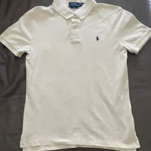 Vit pikétröja Polo Ralph Lauren L - Klassisk vit pikétröja från Polo Ralph Lauren  Storlek 14–16 L i barnstorlek(Slim Fit).  Snygg passform och broderad logga på bröstet.