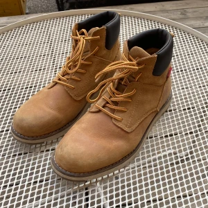 Levi's bruna boots i skinn, strl 40 - Boots från Levi's ”JAX PLUS - Snörstövletter - medium yellow”. Klassisk rund tå, snörning och svart vadderad kant upptill för extra komfort. Perfekta för höst och vinter, snygga till både jeans och cargo.