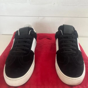 Valentino Garavani sneakers svart/vit mocka - Svarta och vita sneakers från Valentino Garavani med klassisk låg siluett. Ovandel i mocka och skinn, svarta snören och vita detaljer. Snygga nitar längs hälen ger en edgy touch. Perfekta för dig som gillar streetstyle med lyxig känsla.