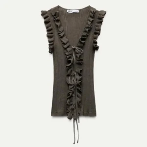 Volangtopp med snörning - Supersnygg grön från Zara med volanger längs v-ringningen och axlarna. Toppen är ribbad, ärmlös och har snörning framtill som ger en unik look. Säljer för den inte passar mig💕. är en m men passar som en s