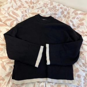 Svart stickad tröja med kontrastkant - Svart stickad tröja från Gina Tricot med breda ribbade muddar och ljusgrå kontrastkant vid ärmslut och nederkant. Tröjan har lång ärm, rund hals och en loose fit som ger en chill vibe. Perfekt för lager-på-lager under kyliga dagar.