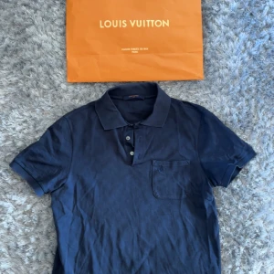 Marinblå Louis Vuitton pikétröja S - Säljer en marinblå piké från Louis Vuitton i bomull. Tröjan har korta ärmar, klassisk krage med knappar och diskret rutmönster i tyget. Bröstficka med broderad LV-logga. Perfekt för dig som gillar exklusiva och stilrena plagg.