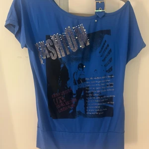 Blå topp från Angie - Cool blå topp med ett stort glittrigt 'FASHION'-tryck och nitar framtill. Storlek M💙